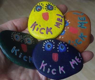 Four hand-painted Kick Me! rocks held in a palm